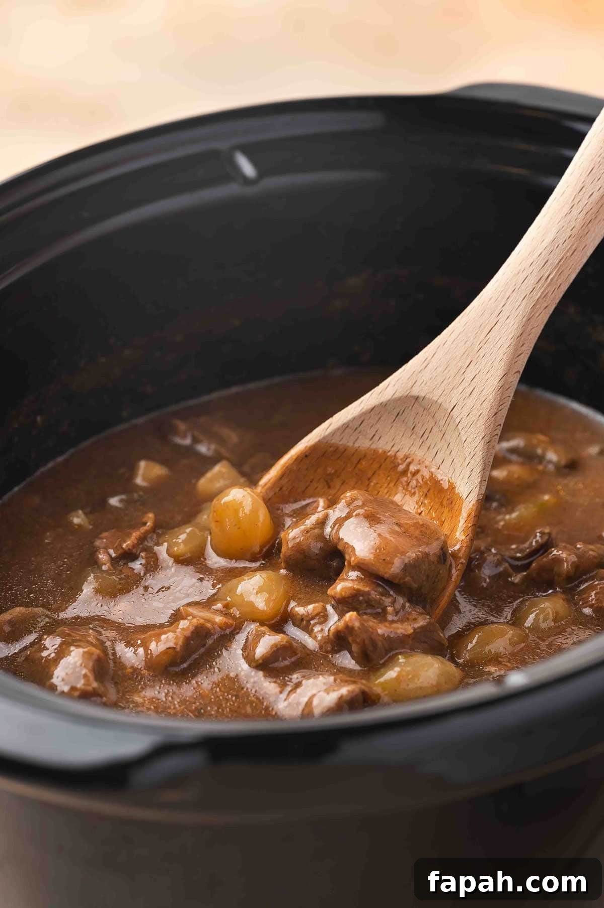 A wooden spoon scooping out beef tips and gravy from a slow cooker.