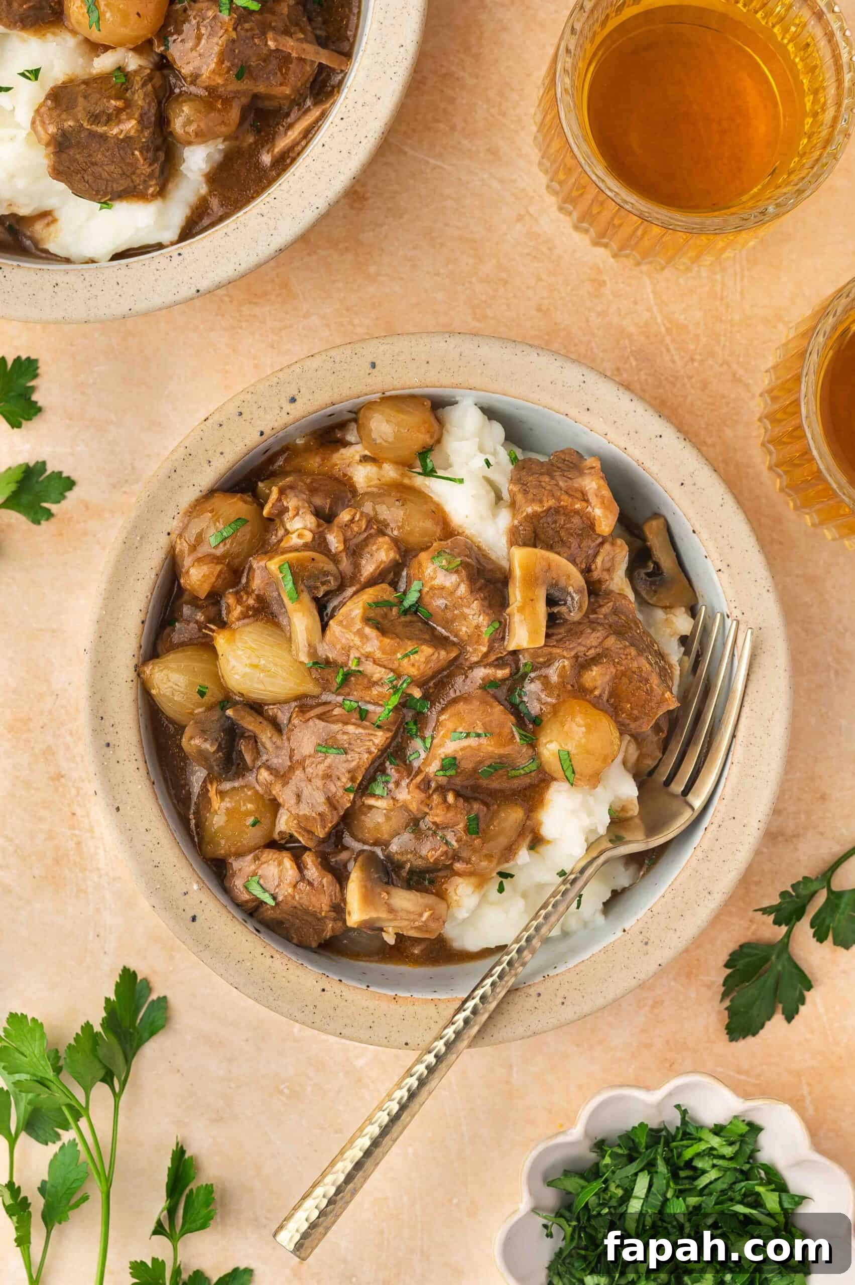 Overhead view of a bowl of crockpot beef tips and gravy over mashed potatoes with a fork garnished with fresh herbs.