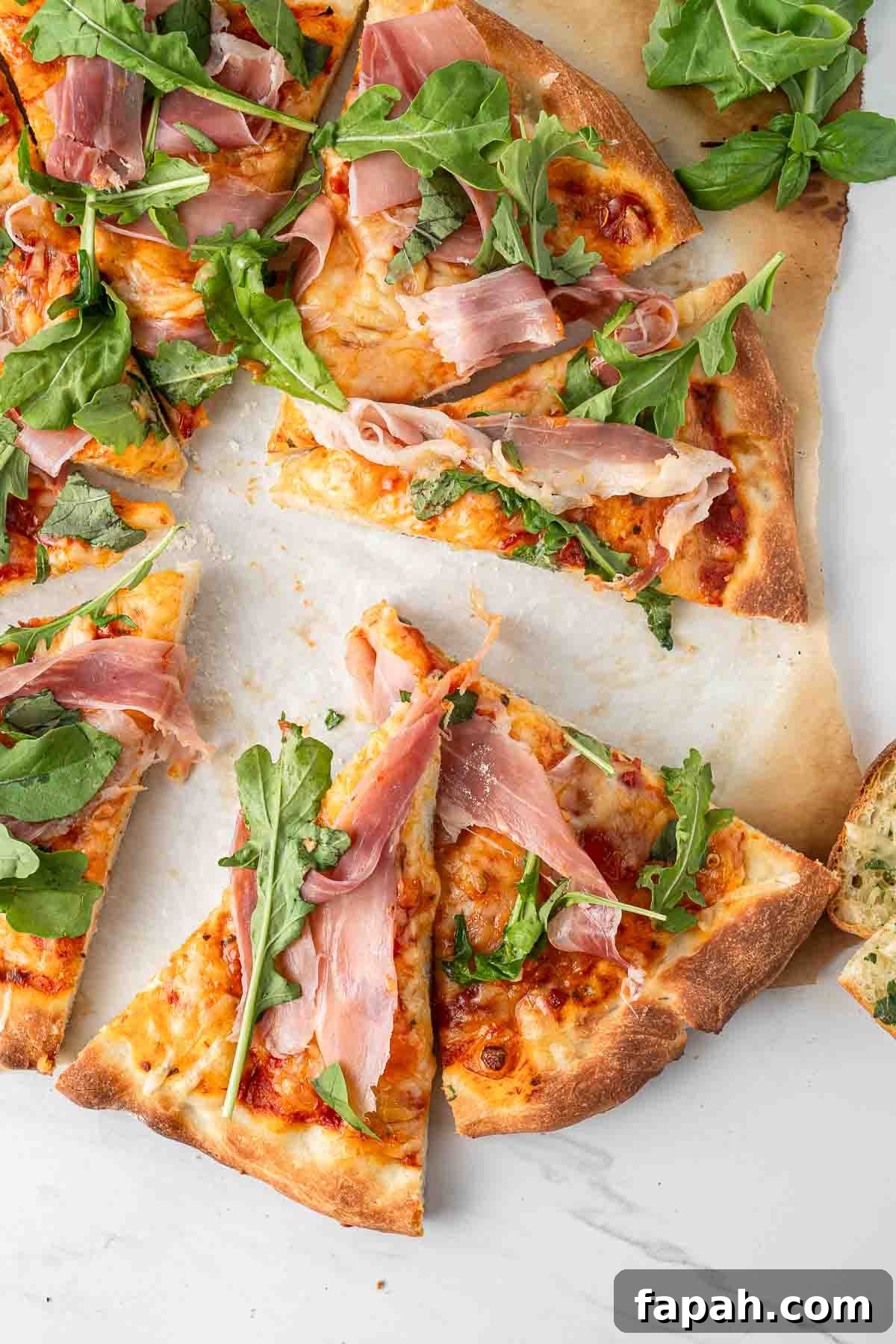 Prosciutto pizza with rocket and basil cut into slices.