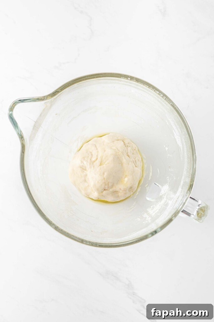 Pizza dough in a large glass mixing bowl.