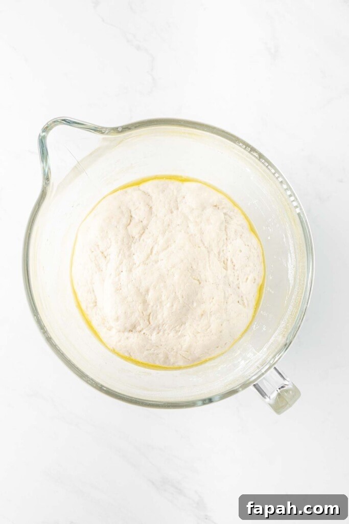 Pizza dough doubled in size in a large glass mixing bowl.