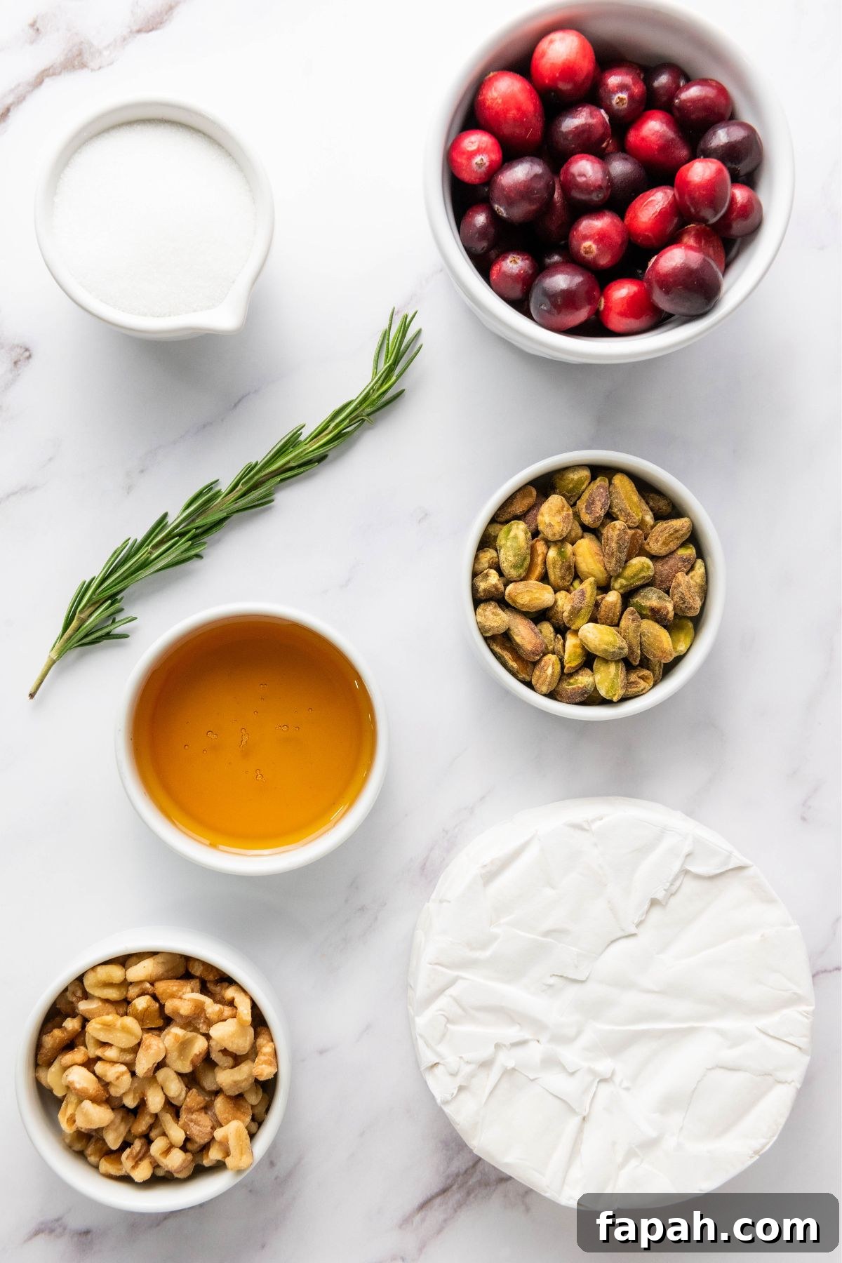 Baked Brie with Honey and Pecans: Warm Party Appetizer 3 Ingredients like brie cheese, cranberries, nuts, and honey, measured out in small bowls on a white marble table.