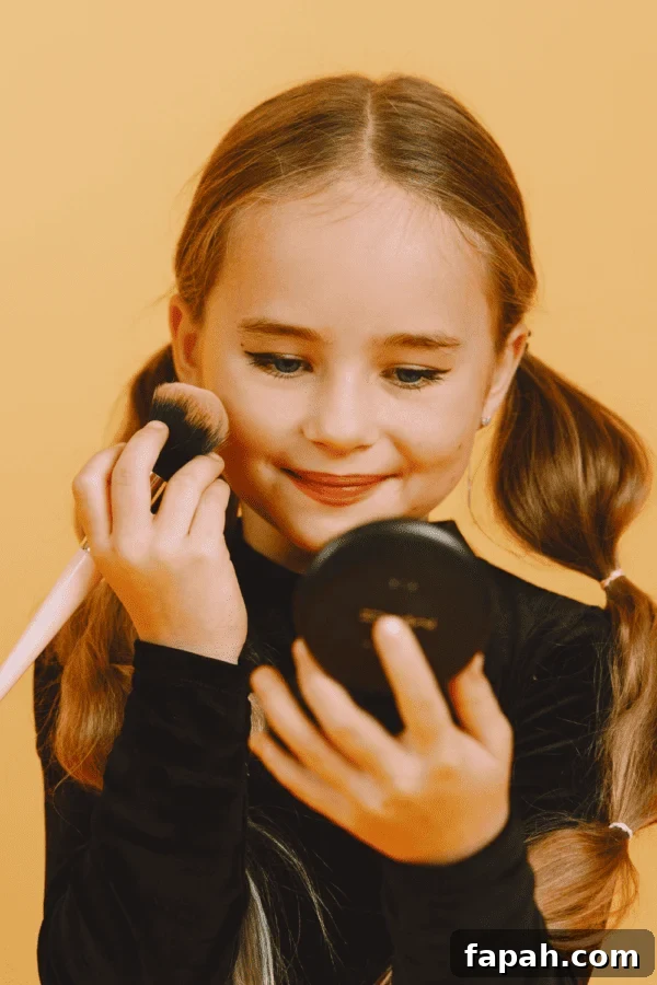 Natural Skincare for Teens & Tweens: 11 Organic, Non-Toxic Brands 2 A young girl with pigtails applies makeup with a brush while holding a compact mirror, smiling against a yellow background.