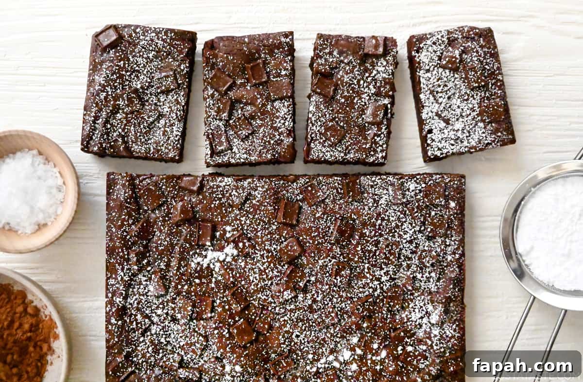 Fudgy Cocoa Brownies Recipe: Rich, Chewy Homemade Treat 12 Fudgy homemade brownies dusted with powdered sugar next to a sifter containing powdered sugar.