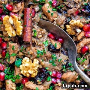 Savory Persian Chicken Stew Recipe (Khoresh-e Morgh) 14 A close-up of Persian chicken stew featuring cooked chicken pieces, walnuts, and pomegranate seeds, garnished with parsley. A cinnamon stick and a metal spoon complete the colorful, textured dish.