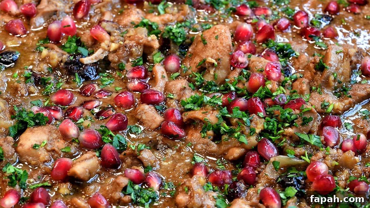Savory Persian Chicken Stew Recipe (Khoresh-e Morgh) 4 Close-up of a vibrant dish featuring chicken pieces cooked in a rich, brown sauce, generously topped with pomegranate seeds and fresh green herbs, creating a colorful and appetizing presentation.