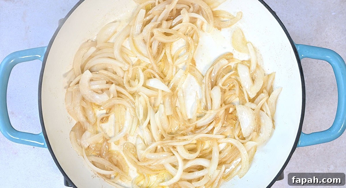 Savory Persian Chicken Stew Recipe (Khoresh-e Morgh) 6 Sliced onions cooking in a white pot with blue handles. The onions are light golden, indicating they are starting to caramelize.
