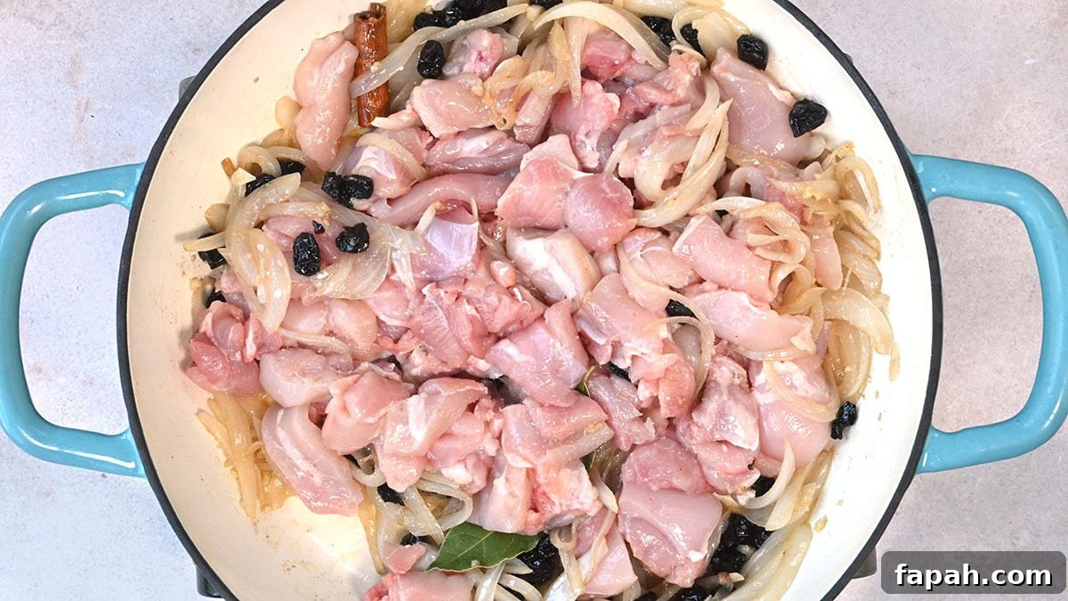 Savory Persian Chicken Stew Recipe (Khoresh-e Morgh) 7 Raw, marinated chicken pieces mixed with sliced onions and small dark berries in a large, round blue-handled pan. The mixture is evenly spread, ready to be cooked.