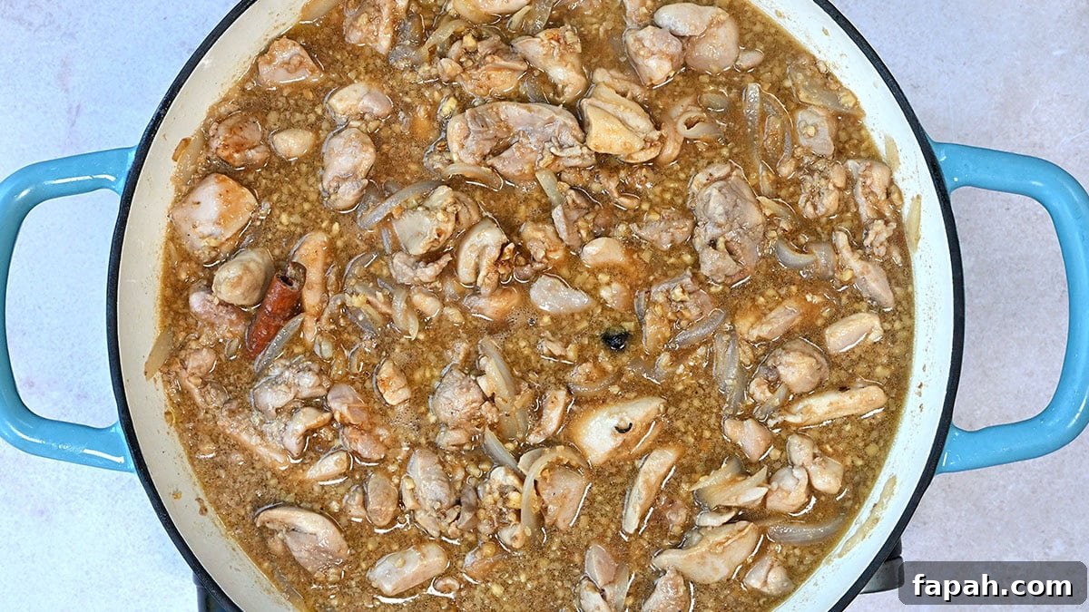 Savory Persian Chicken Stew Recipe (Khoresh-e Morgh) 8 A blue-handled pot filled with a chicken stew containing chunks of chicken, ground walnuts, and visible pieces of onion. The mixture appears to be simmering, with small bubbles on the surface.
