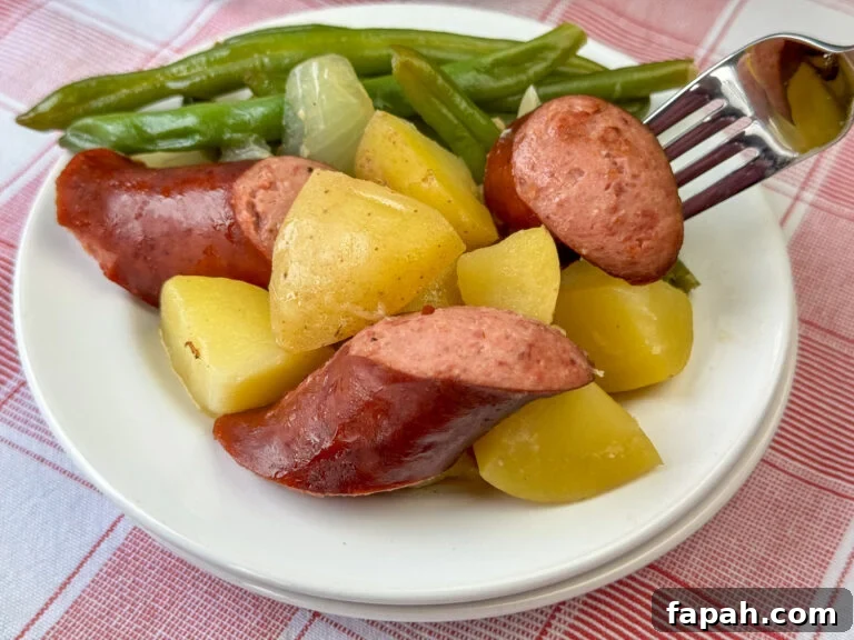 Close up fork in a pieces of savory smoked sausage next to tender cubes of potatoes with green beans and onions on a stack of white plates.