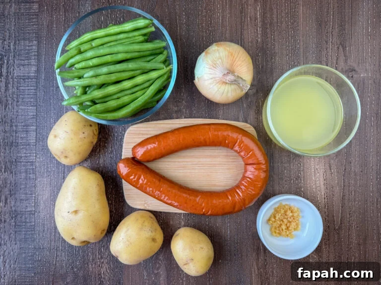 Ingredients to make Instant Pot Sausage and potatoes are smoked sausage, onion, chicken broth, minced garlic, potatoes and green beans on a wooden counter.