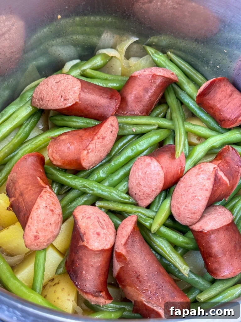 Smoked sausage on layers of potatoes and green beans in an Instant Pot.