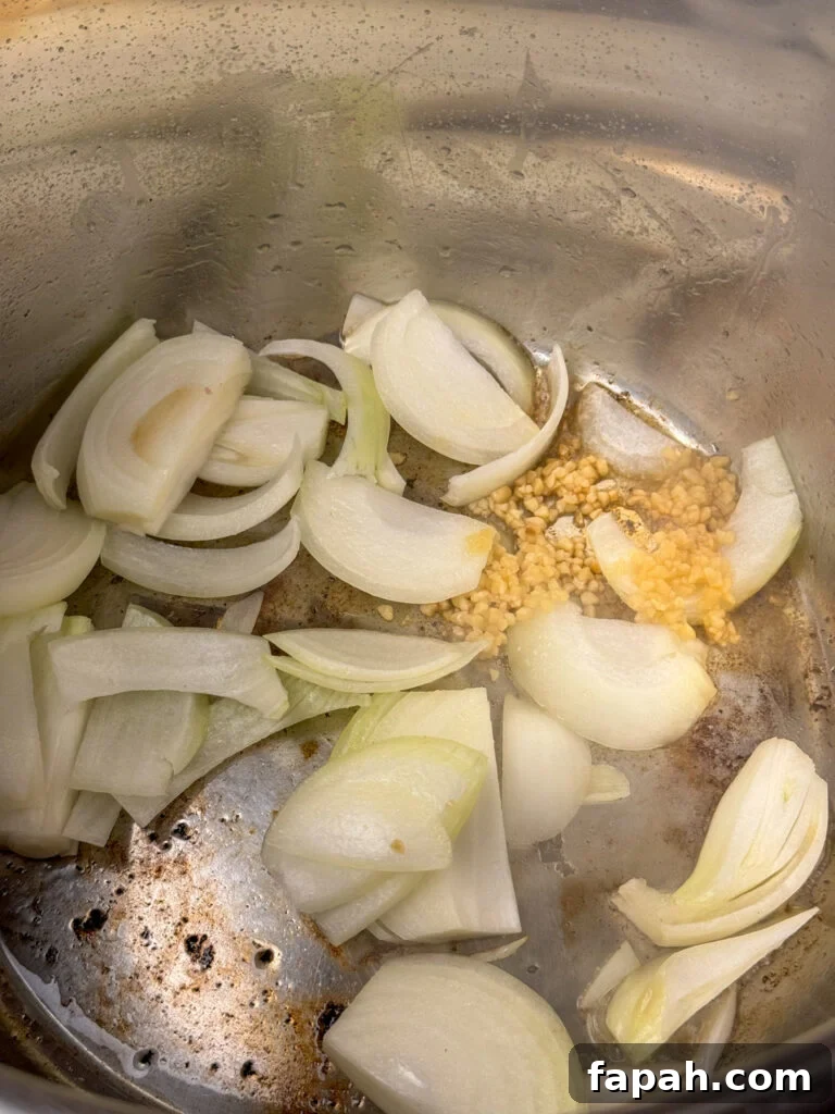 Fresh chunks of sweet onion added to vegetable oil with minced garlic in an Instant Pot with bits of browned sausage in the bottom.