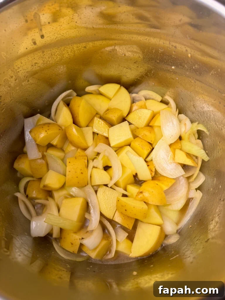 Chunks of potatoes added to slices of onions and tender garlic in an Instant Pot.