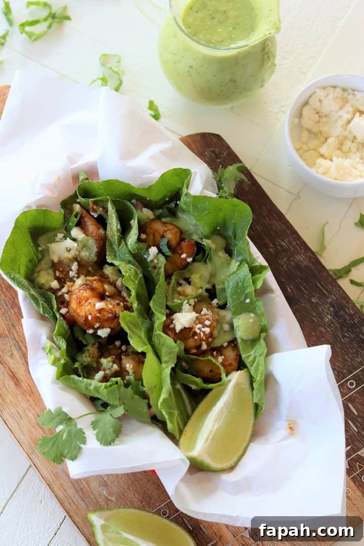 Portrait image of shrimp taco served in a basket lined with white parchment. A side of lemon wedges, queso fresco cheese, and the avocado lime dressing are on the side.