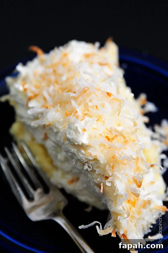 Closeup of blue plate and fork with Coconut Cream Pie covered in toasted coconut on top of thick whipped cream.