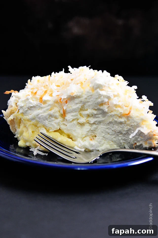 Side view of blue plate holding coconut cream pie, with thick coconut custurd and pillowy homemade whipped cream.