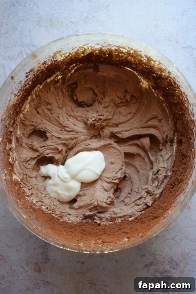 Adding heavy cream to chocolate buttercream frosting.