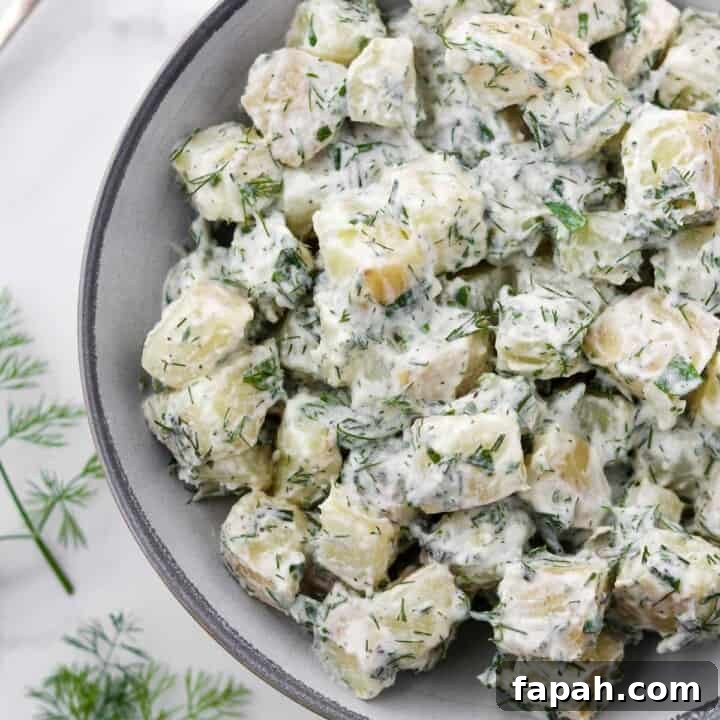 Creamy Herbed Potato Salad in a bowl next to a spoon and dill sprigs.