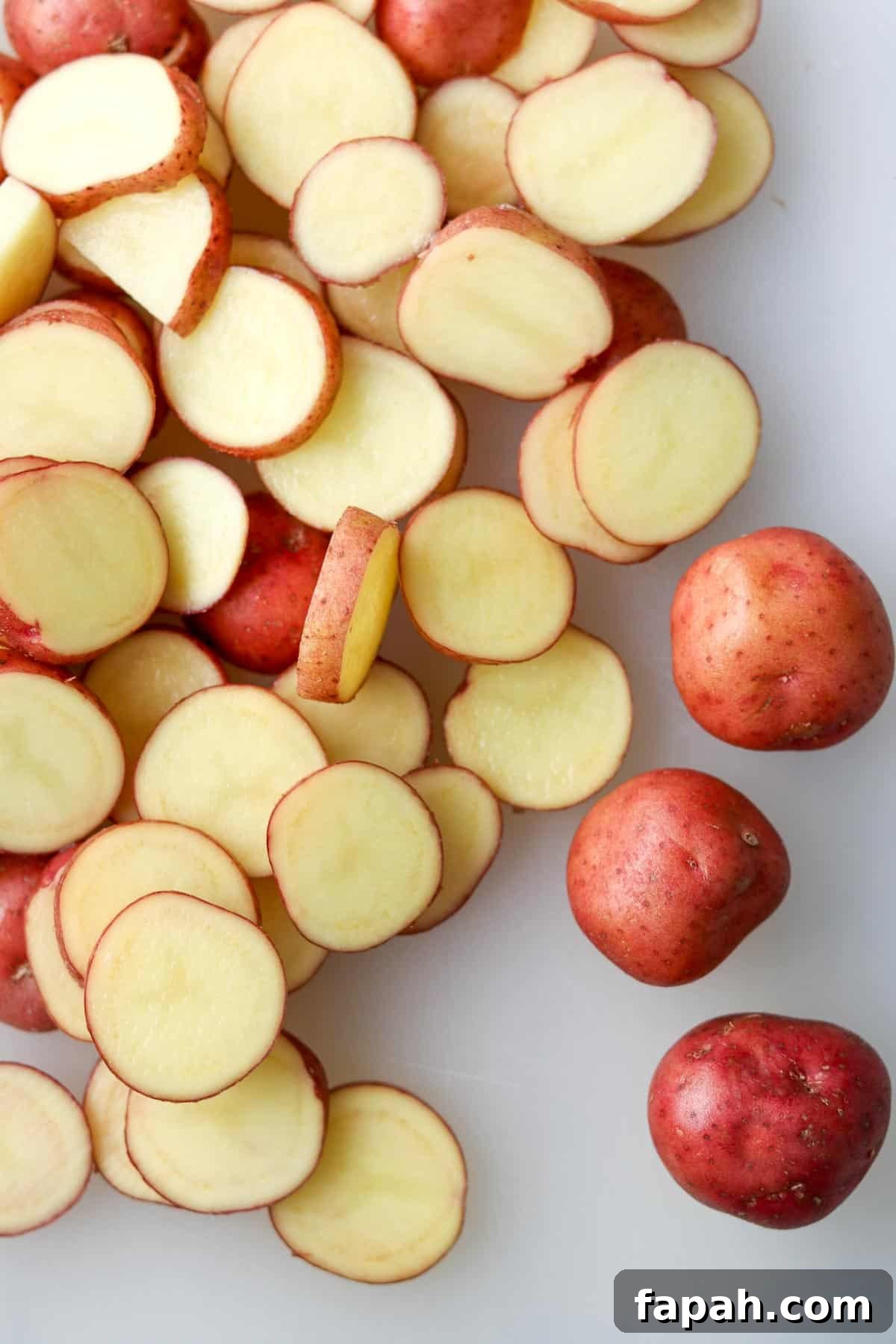 Sliced baby red potatoes on a white cutting board.