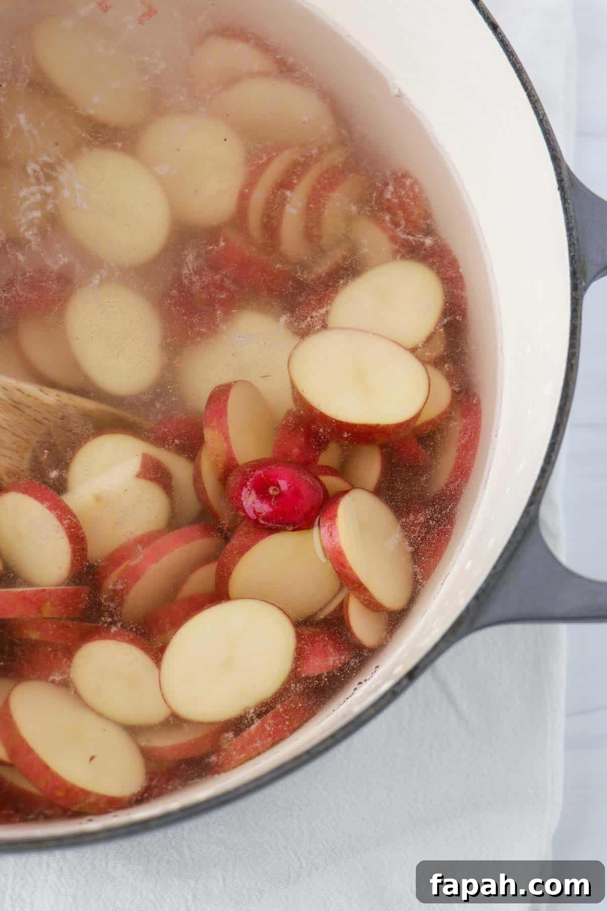 Sliced baby red potatoes cooking in a pot of water.