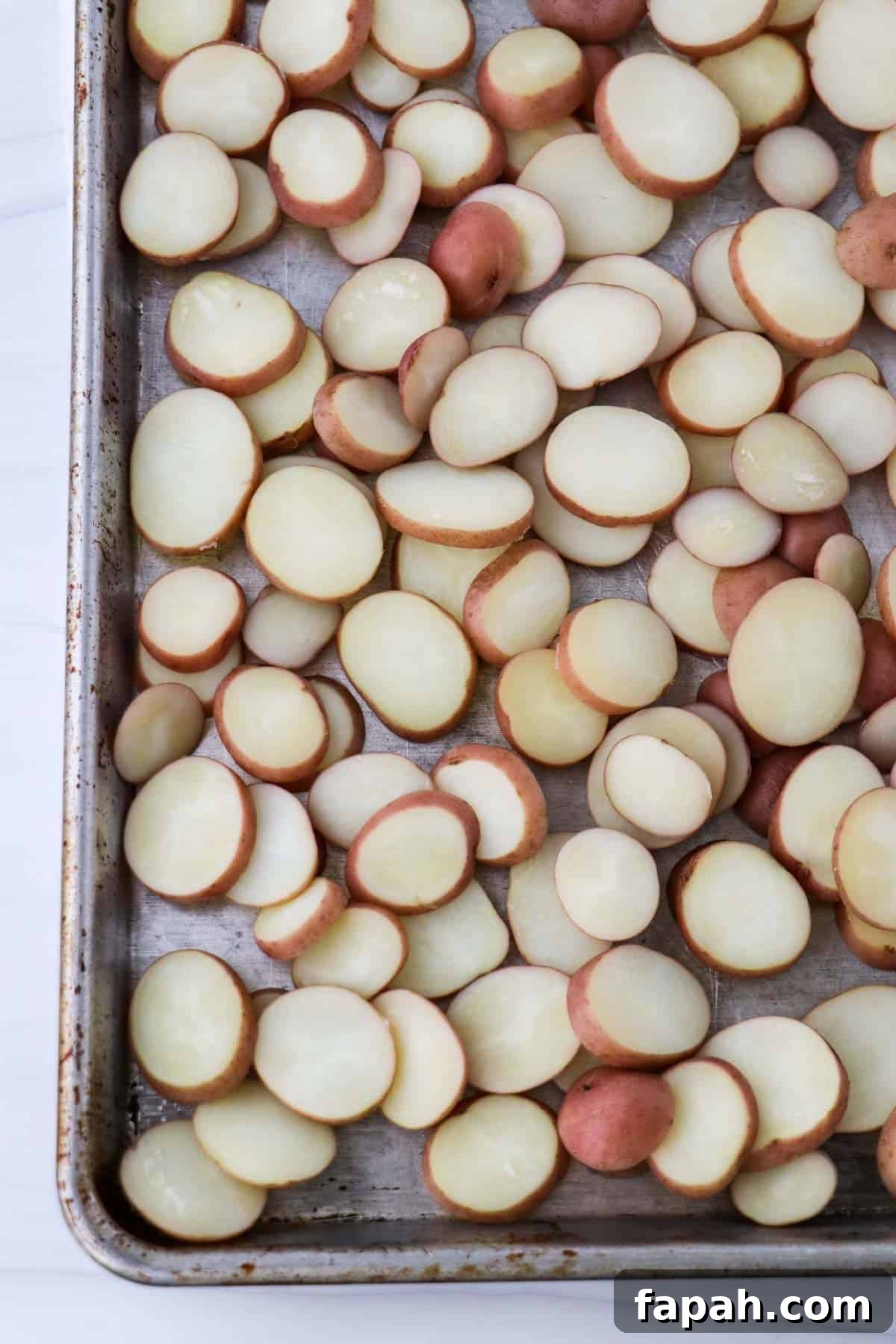 Sliced baby red potatoes on a baking sheet.