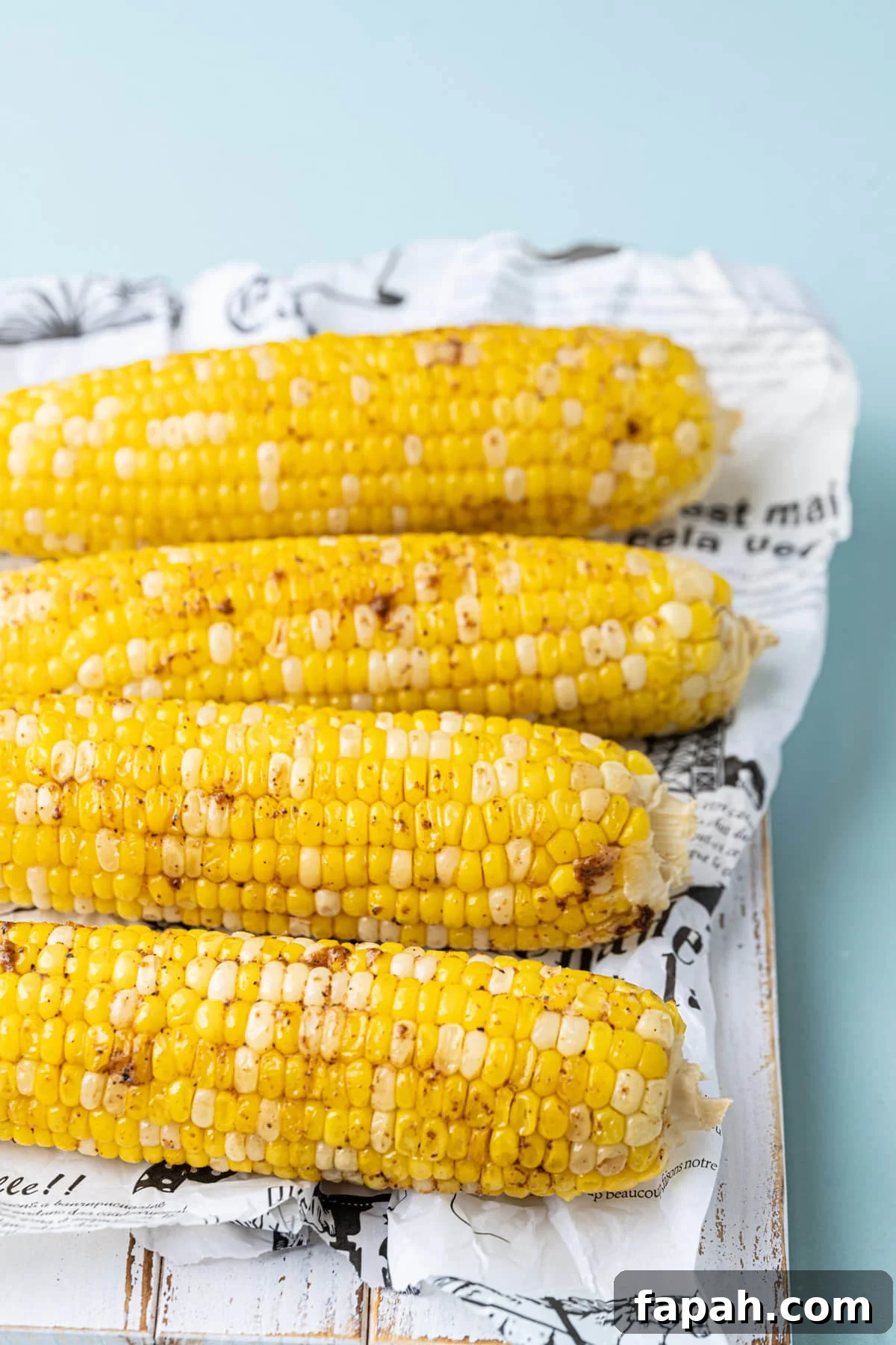 4 ears of roasted corn sprinkled with Cajun seasoning lined up on a board.