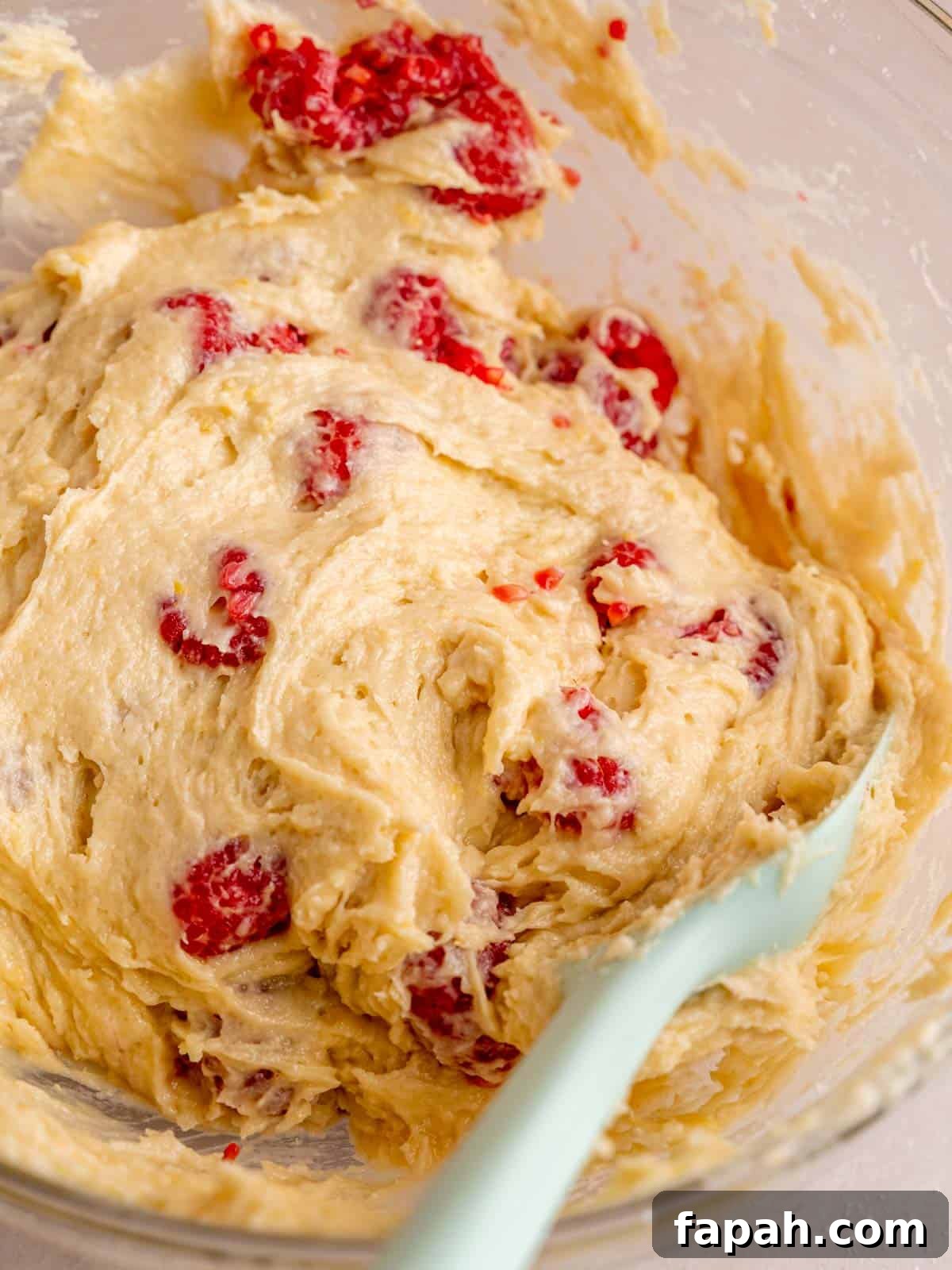 Lemon Raspberry Muffins with Zesty Glaze 8 Folding fresh raspberries into lemon muffin batter using a spatula.