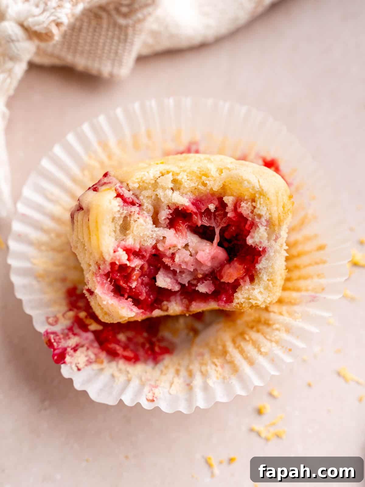 Lemon Raspberry Muffins with Zesty Glaze 10 A lemon muffin with raspberries that has a bite taken out of it.