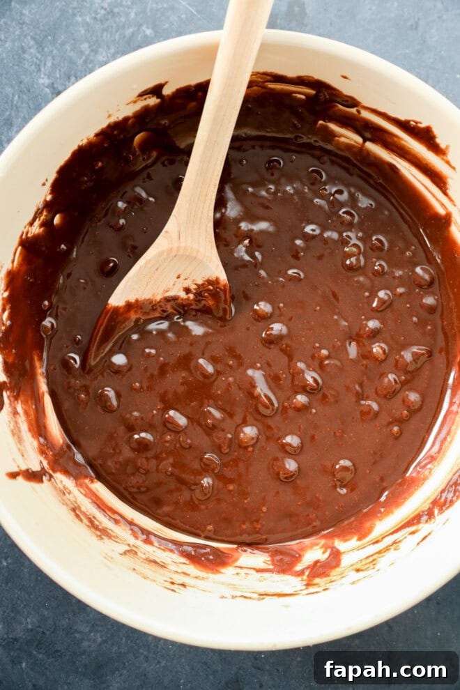 Pumpkin Swirl Brownies with Spiced Cream Cheese Filling 4 A bowl of brownie batter with a wooden spoon resting inside. The batter is thick and glossy with some air bubbles visible on the surface. The bowl sits on a dark countertop.