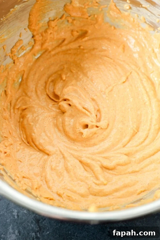 Pumpkin Swirl Brownies with Spiced Cream Cheese Filling 5 A metal mixing bowl filled with creamy, light brown batter, swirled smoothly, sitting on a dark countertop.