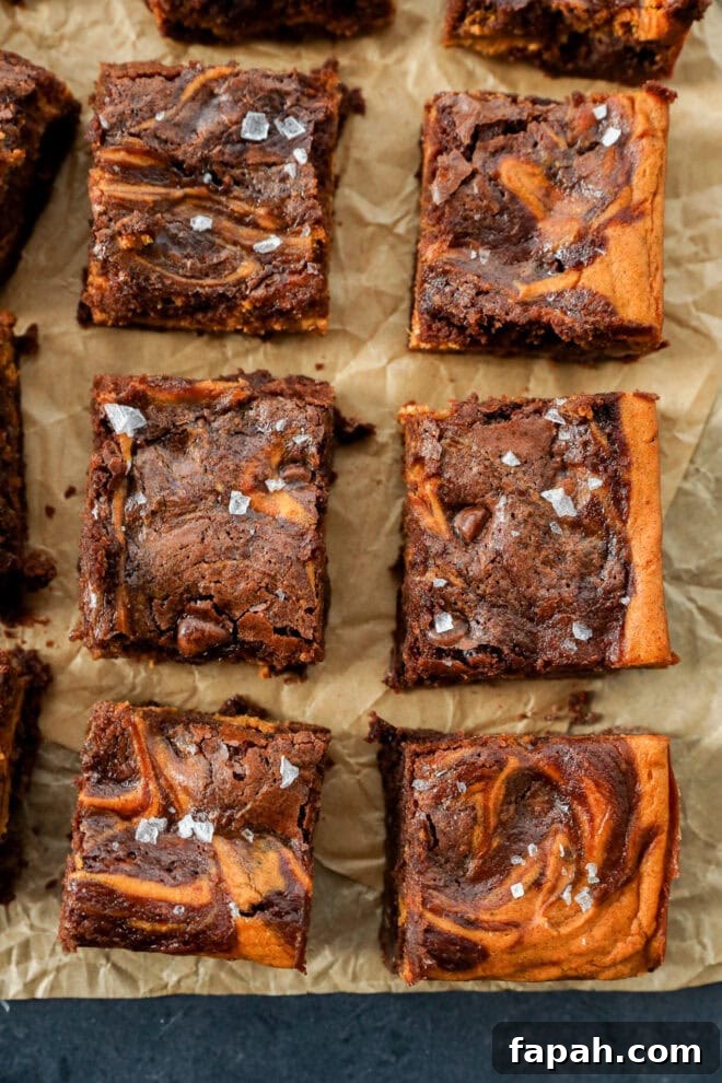 Pumpkin Swirl Brownies with Spiced Cream Cheese Filling 7 Nine chocolate brownies with a marbled pattern and sprinkled sea salt on top, arranged neatly on parchment paper.