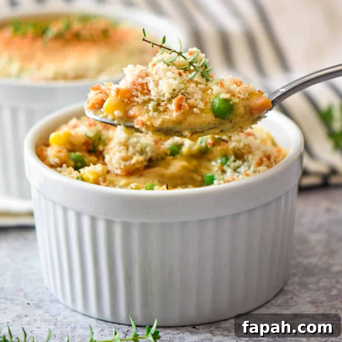 A spoon scooping up chicken pot pie filling from a ramekin dish.