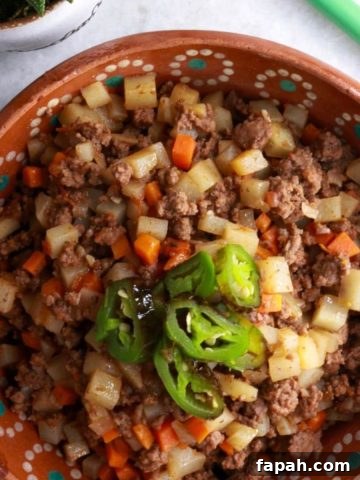 Bowl of picadillo con papas topped with sliced jalapeños