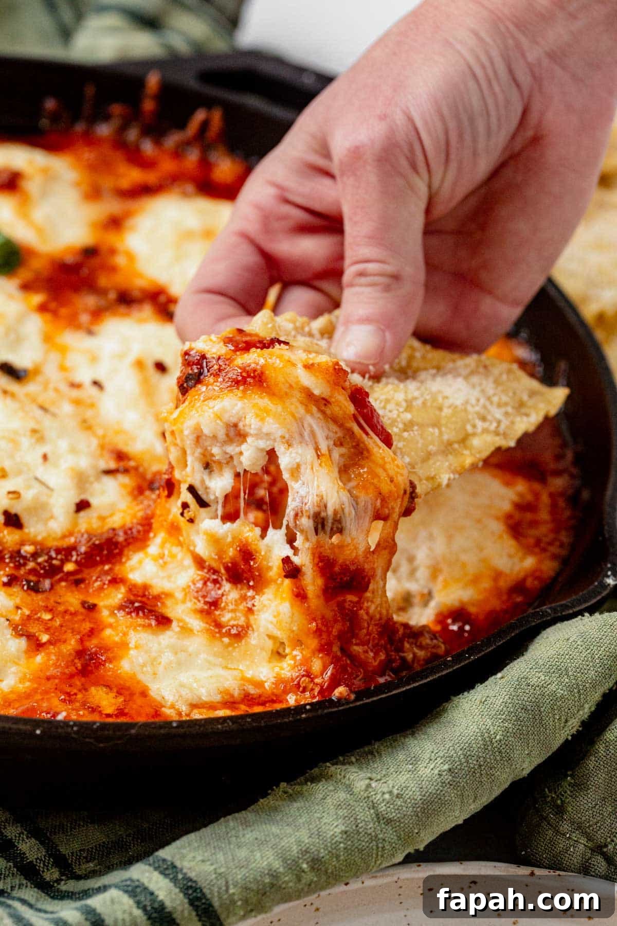 scooping lasagna dip from a skillet.