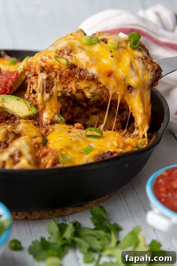 a slice of tamale pie being lifted out of a cast iron skillet with cheese stringing off