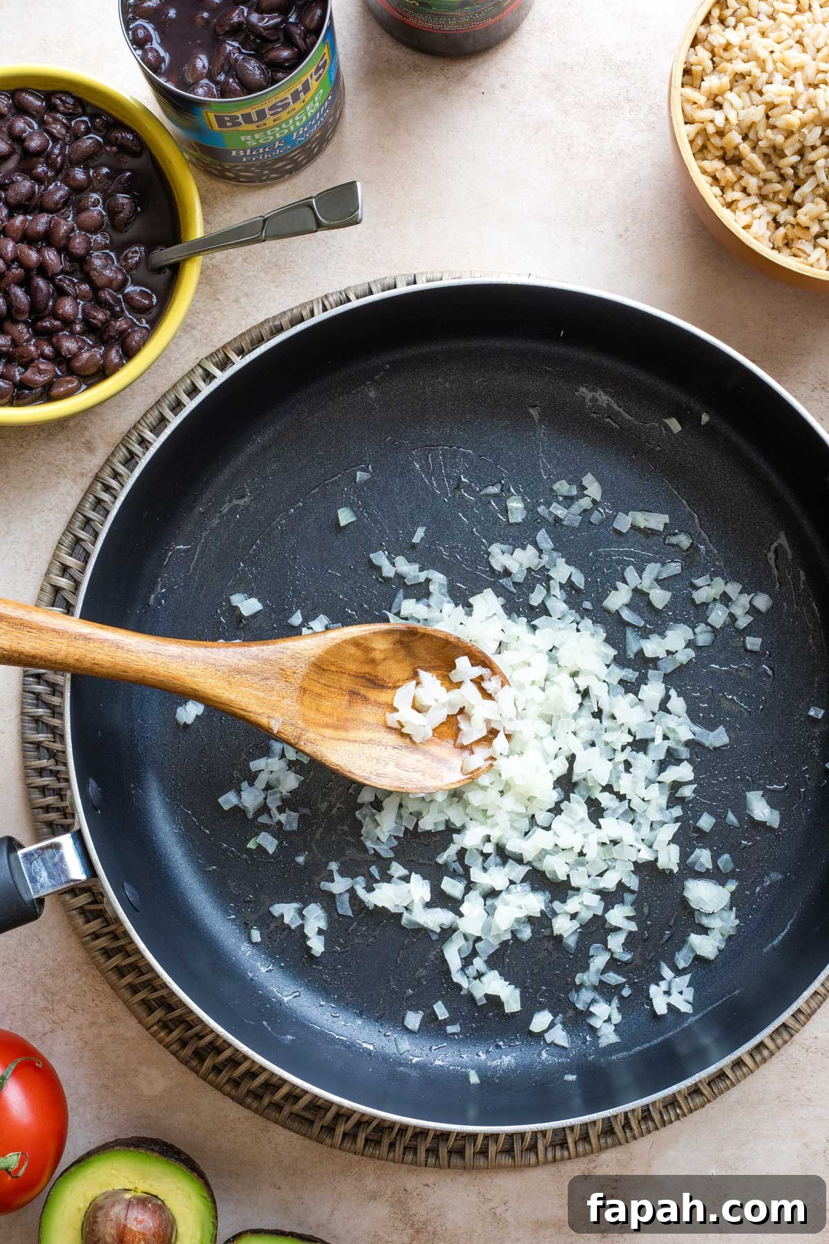 Overhead of Step #2 with diced onions added to the skillet and a wooden spoon stirring them.