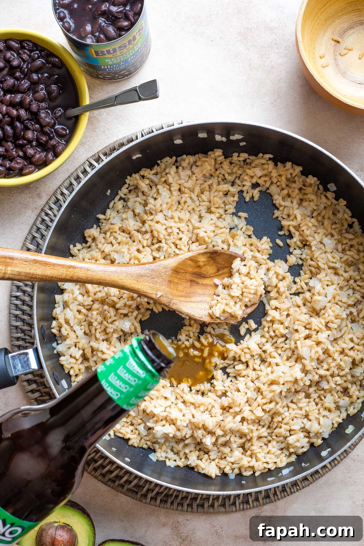 Overhead of recipe step #4 with Lizano Sauce being poured from bottle into the rice in the skillet.