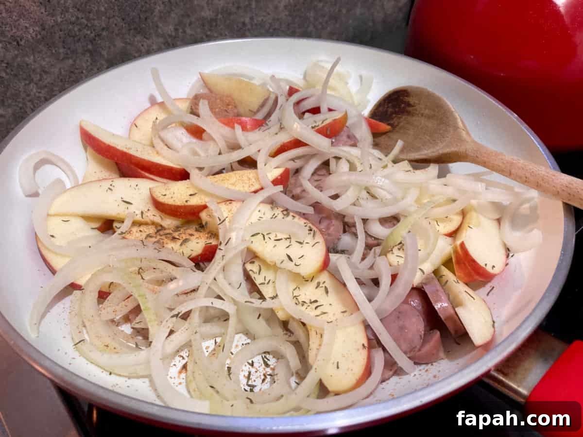 Apple slices, sliced onion and sausage in skillet with wooden spoon.
