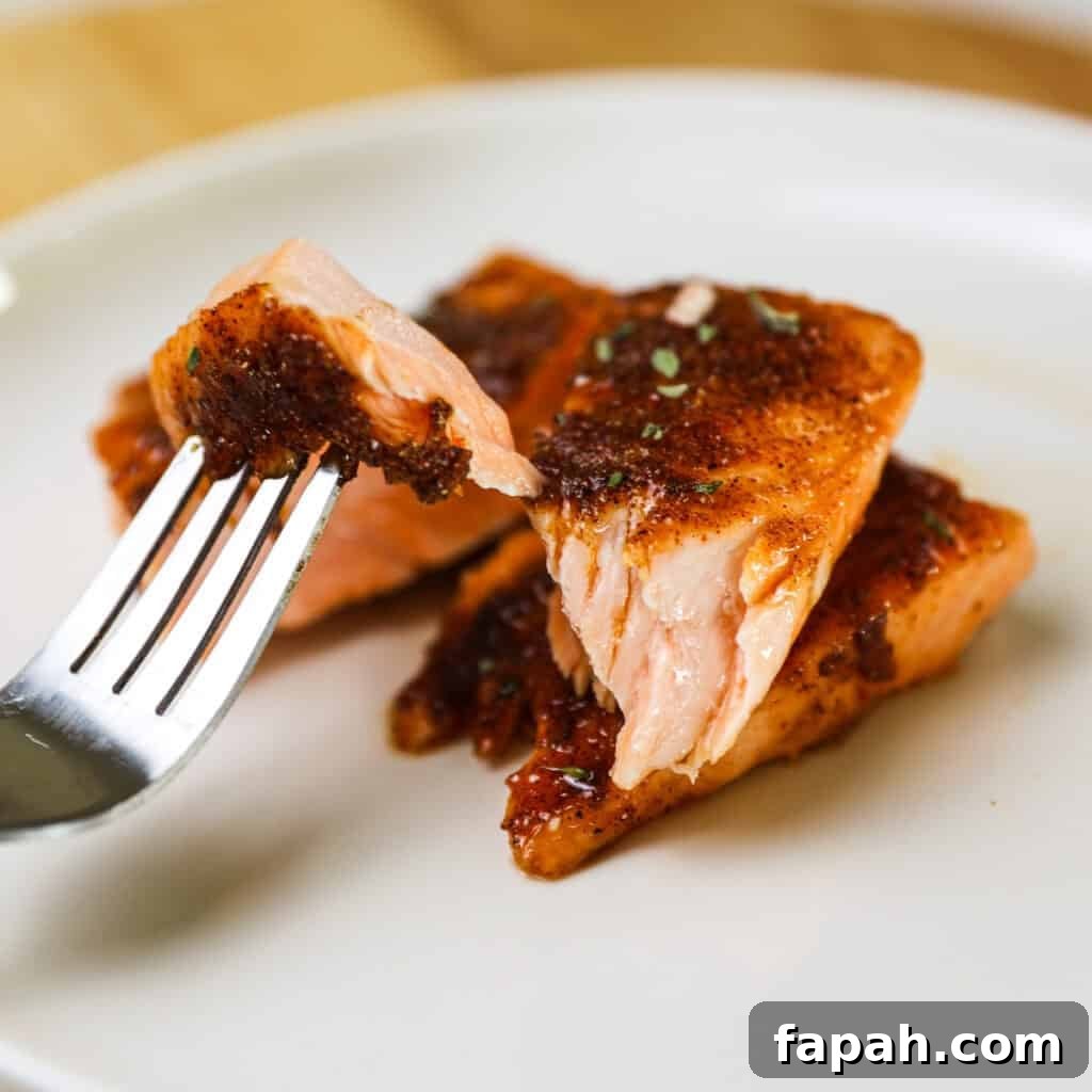 Sweet and Spicy Salmon in the Air Fryer: Quick Crispy Recipe 6 A fork with a flaked off piece of air fried salmon on a dinner plate. spicy air fryer salmon.