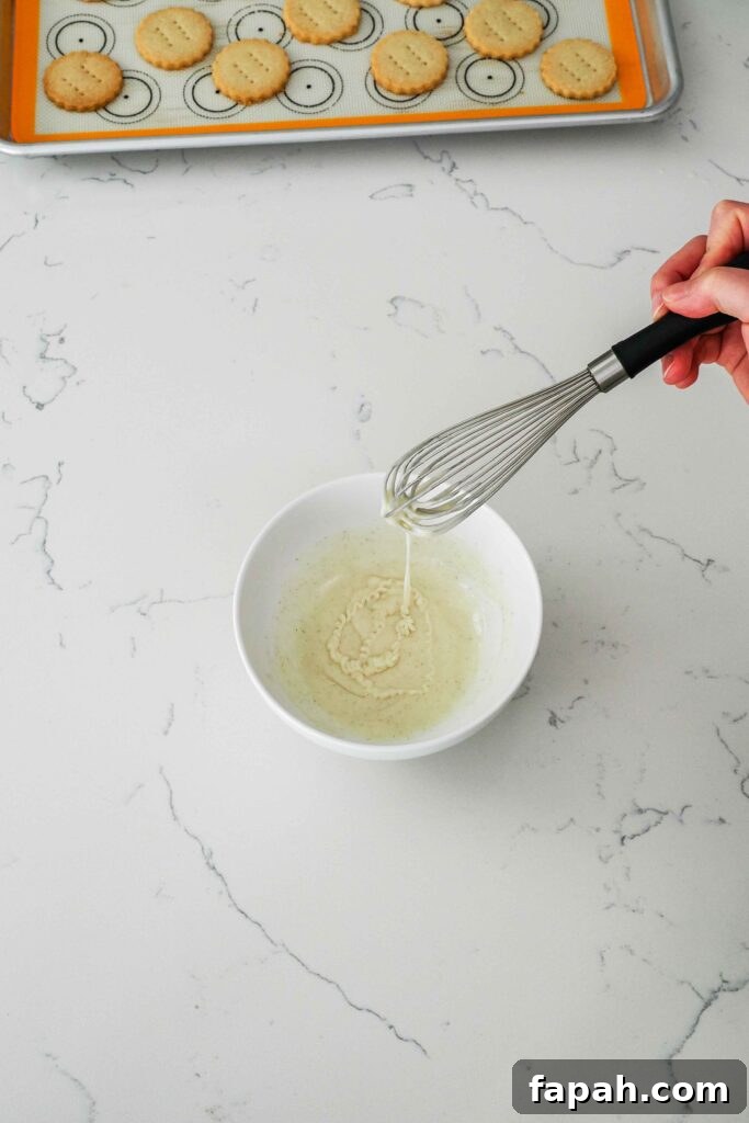 Vanilla glaze drizzles off a whisk and into a bowl.