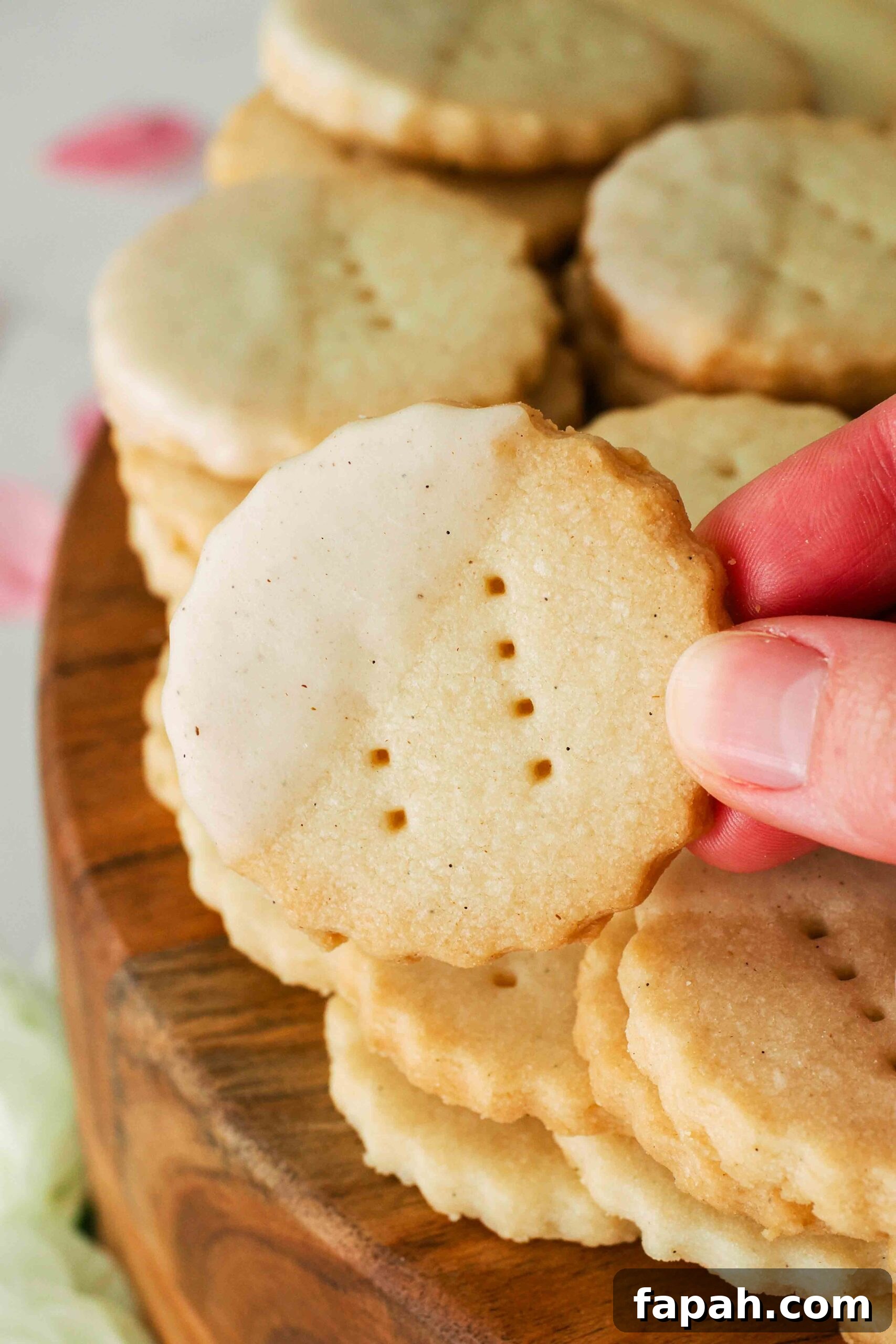 A hand holds up a glazed vanilla shortbread cookie.