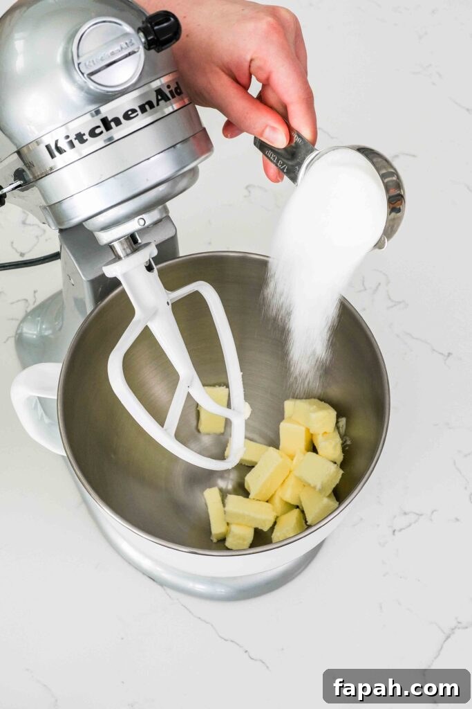 A hand pours granulated sugar into a mixing bowl with butter.