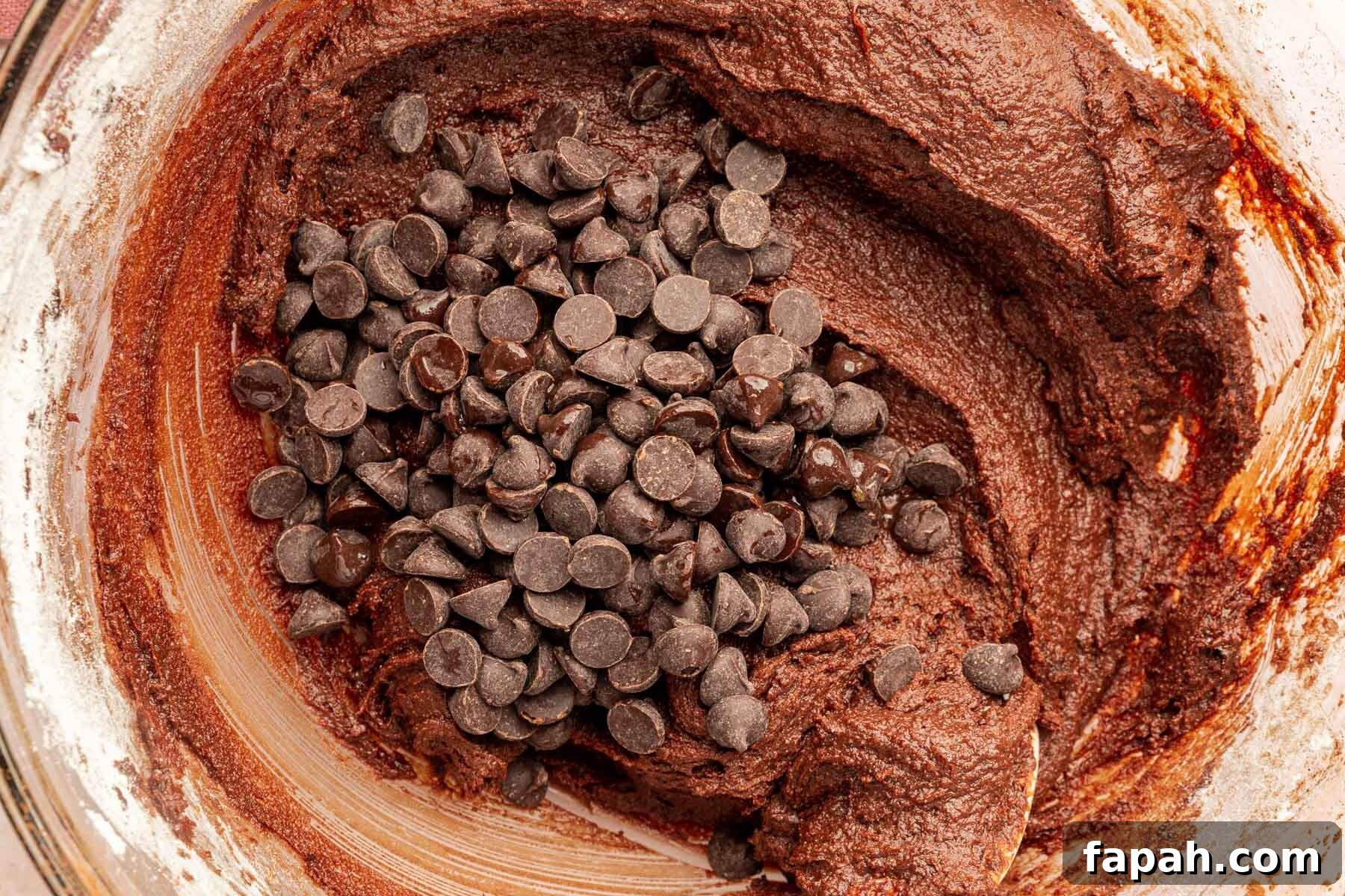 A closeup of gluten-free batter in a mixing bowl topped with a pile of semi-sweet chocolate chips.