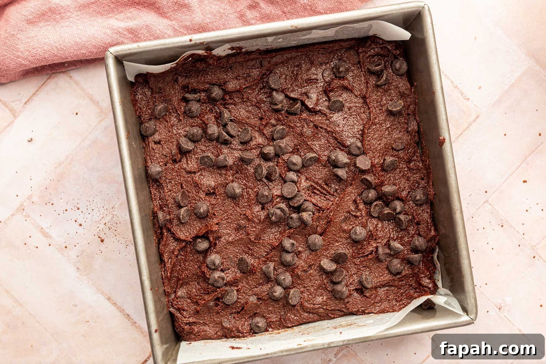 A square baking pan filled with brownie batter and topped with semi-sweet chocolate chips before baking in the oven.