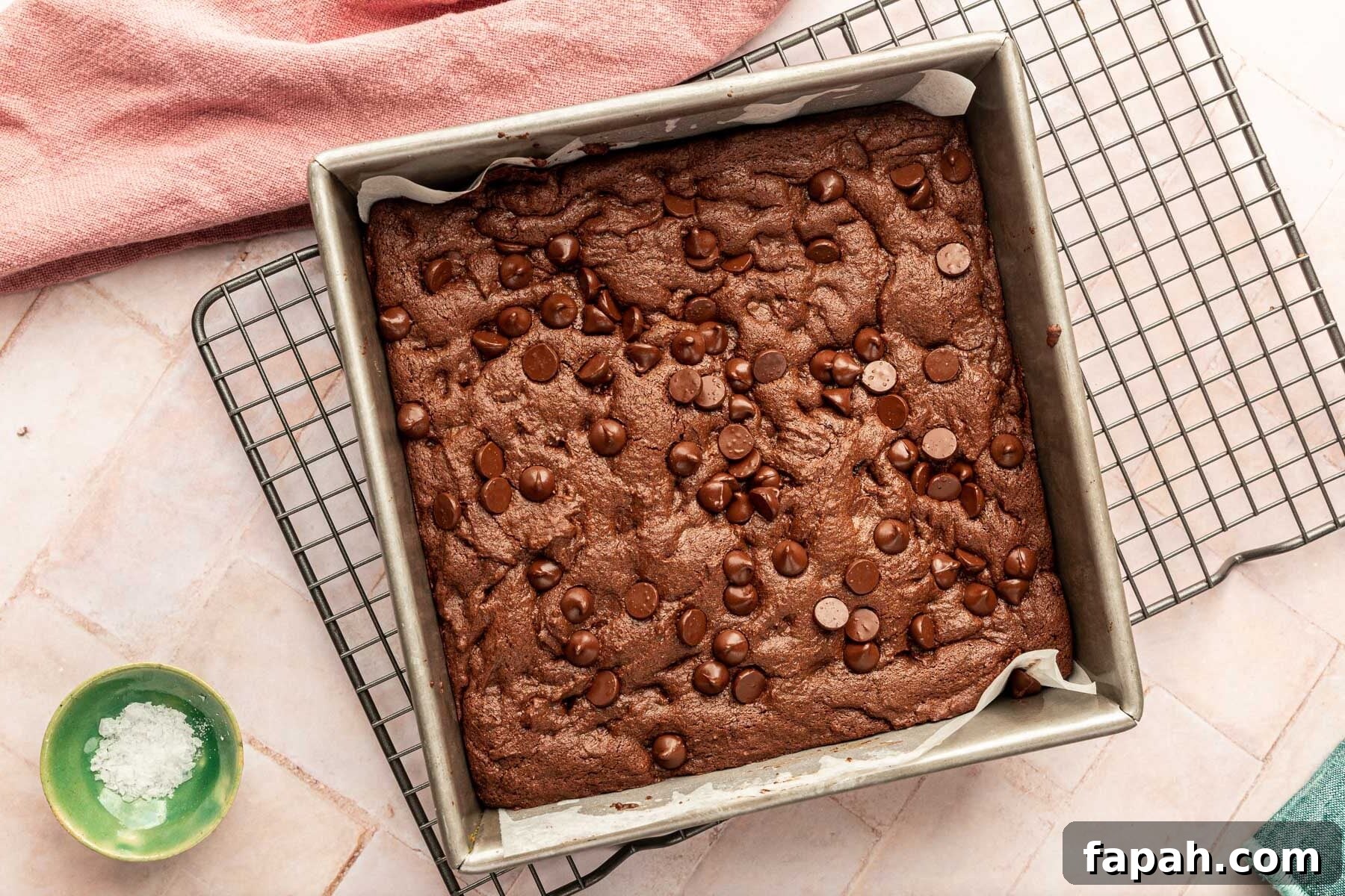 A square baking pan filled with baked gluten-free brownies on top of a pink background.