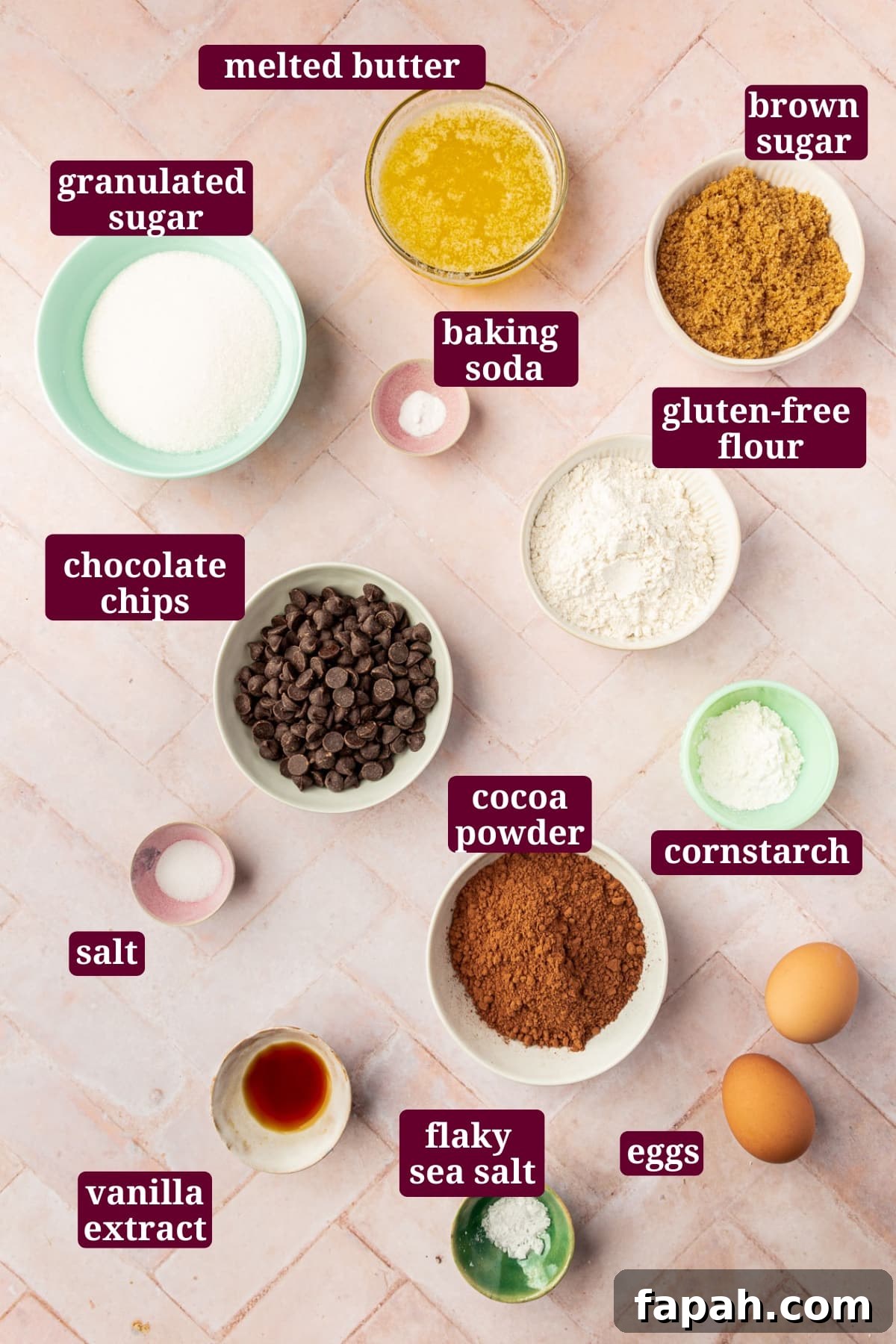 An overhead view of ingredients in small bowls to make gluten-free brownies, including granulated sugar, melted butter, brown sugar, baking soda, gluten-free flour, chocolate chips, cocoa powder, cornstarch, eggs, and vanilla extract.
