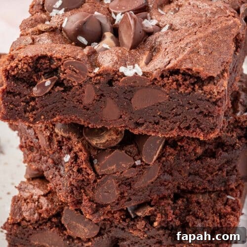 A stack of three gluten-free brownies topped with semi-sweet chocolate chips and flaky sea salt.