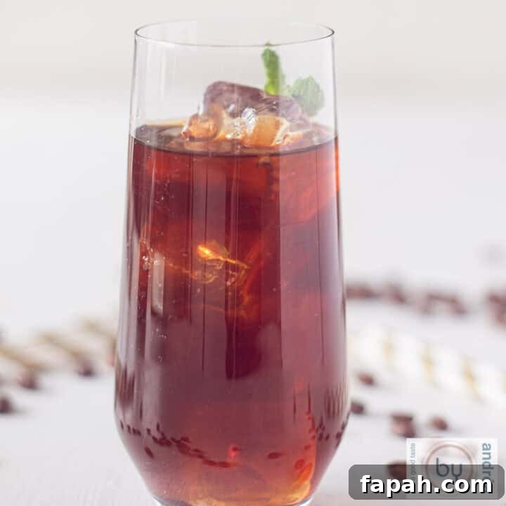 A square photo of a glass filled with Mexican iced coffee on a white surface. Coffee bean and straws lie around it
