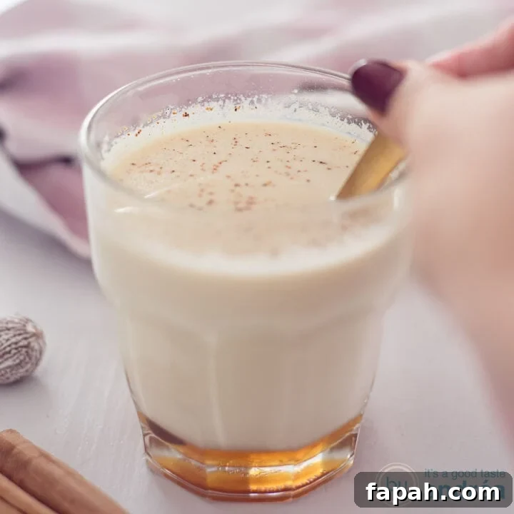 A square photo with a glass in the middle filled with chai tea with milk and honey. A golden spoon stirs the glass.